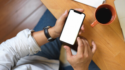 Top view of male hand using smartphone on wooden worktable