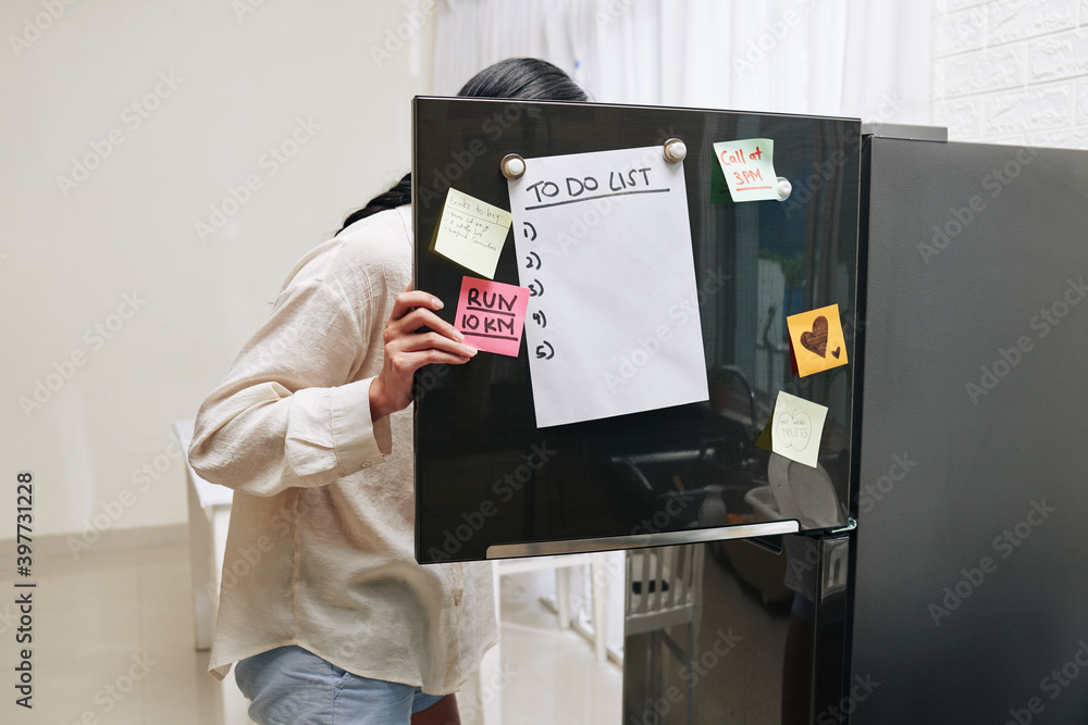 Wall mural young woman opening fridge door covered with motivating stickers