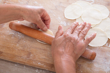 The chef rolls the dumpling wrapper on the cutting board with a rolling pin in hand