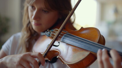 Girl playing violin at home. Violinist playing chords on musical instrument