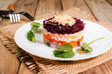 Traditional Russian herring under a fur coat in transparent plate with parsley. Rustic style.