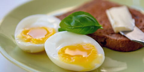 Two soft-boiled egg halves on a plate. Basil leaf, toast and butter. Close up.