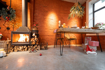 Fototapeta na wymiar Fireplace area of a beautiful loft-style interior with real brick and concrete floors decorated for the New Year holidays. The concept of home comfort