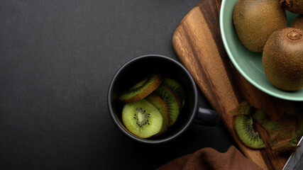 Sliced fresh kiwi fruit in ceramic cup on kitchen table with whole kiwi fruit in a bowl