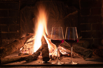 Two glasses of red wine and a lit fire
