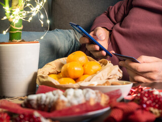 Closeup view of man with mobile phone sitting near Christmas decorated table 