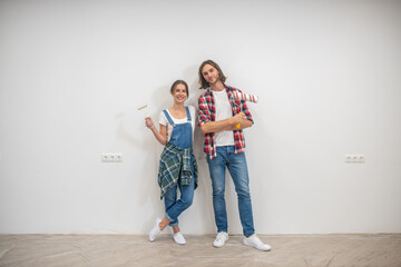Young couple standing near the wall with paint rollers and hands