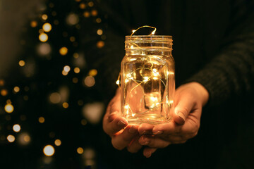 Woman holding holiday led light garland in jar. Christmas, new year holiday celebration concept.