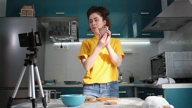 A young smiling woman shoots a video on her smartphone showing cooked gingerbreads. The concept of streaming and cooking vlogs