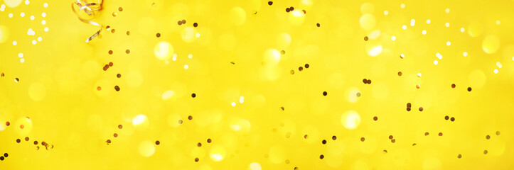 New year, Christmas background. Golden shiny glitter, sparkles, light bokeh on yellow background. Banner with copy space. Festive backdrop for greeting card