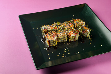 Sushi set served on a black square plate over bright pink background. Traditional Japanese cuisine, sushi rolls close up