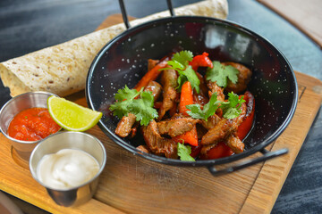 Vegetables and meat in wok pan served with lavash bread and different kinds of sauce. Close up.