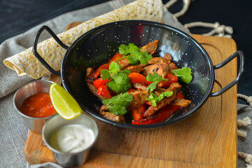 Vegetables and meat in wok pan served with lavash bread and different kinds of sauce. Close up.