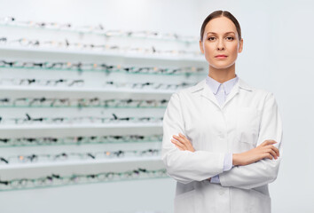 medicine, vision and healthcare concept - female eye doctor or ophthalmologist in white coat over glasses at optical store background