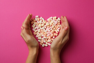 Female hands and heart made of marshmallow on pink background