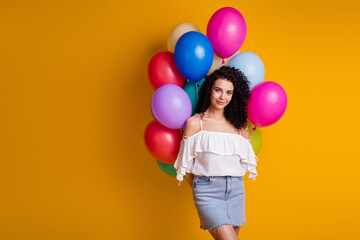 Fototapeta na wymiar Photo of pretty cute brown curly girl hold many balloons behind back wear top skirt isolated on yellow color background