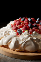 food, culinary, baking and cooking concept - close up of pavlova meringue cake decorated with berries on wooden serving board