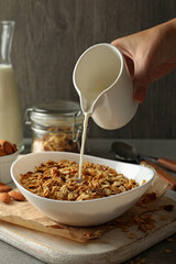 Female hand pour milk in bowl with granola
