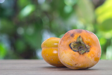 Two ripe sweet persimmons are placed on the table in front of the blurred green background