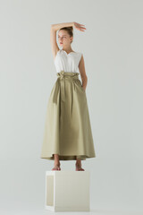A woman stands in the studio on a white cube. Clothes - a long green skirt and a white T-shirt. The...