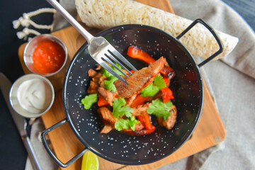 Vegetables and meat in wok pan served with lavash bread and different kinds of sauce. Close up.