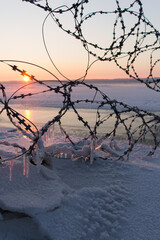 winter landscape frozen river Volga at dusk of sunset. frozen barbed wire with icicles. Soft focus