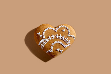 Festive bakery. Lovely pastry cookie. Holiday surprise. Homemade white ornament icing gingerbread heart biscuit isolated on beige pastel.