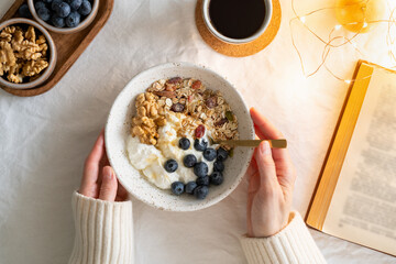 Top view book and Christmas healthy lifestyle breakfast with granola muesli and yogurt in bowl on white table background, cereal grain food with nuts seed. Organic morning diet meal 