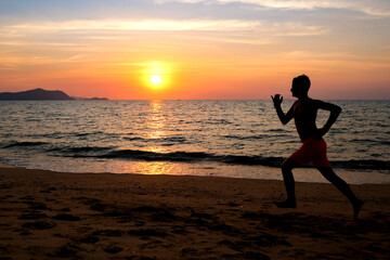Fototapeta na wymiar Silhouette of a young man running at the beach at sunrise with the sun in the background. Staying fit and healthy banner