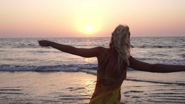 Beautiful young woman dancing and having fun on the sea beach against the backdrop of the sunset