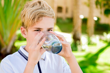 Young caucasian boy drinking clear fresh mineral water, outdoors during summer time. Health concept.