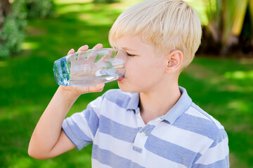 Young caucasian boy drinking clear fresh mineral water, outdoors during summer time. Health concept.