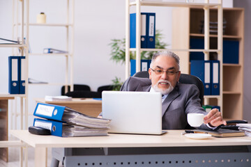 Old male employee drinking coffee in the office