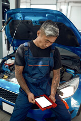 Mechanic looking at tablet screen while leaning on machine