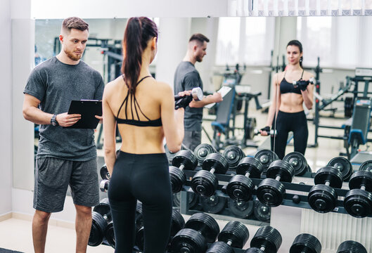 Beautiful young woman with her personal trainer at the gym discuss the progress on a clipboard held by the man. Healthy lifestyle.