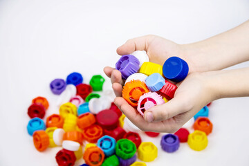 In children's palms there are plastic bottle caps against the background of other multi-colored plastic bottle caps. Ecology and recycling concept.