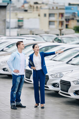 Female car dealership manager showing cars to customer and helping him to choose the best one