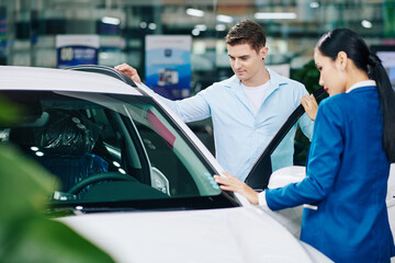 Dealership manager opening automobile door to show car interior to customer