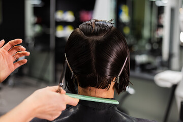A professional girl hairdresser makes a client haircut. The girl is sitting in a mask in beauty the...