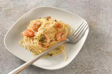 Appetizer spaghetti with shrimps, garlic and herbs, Mediterranean seafood on a small plate, rustic gray background with copy space, selected focus