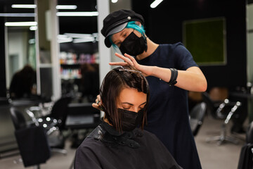 A professional girl hairdresser makes a client haircut. The girl is sitting in a mask in beauty the...