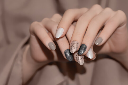 Female hands with beige nail design. Glitter gray nail polish manicure. Woman hands on brown fabric background