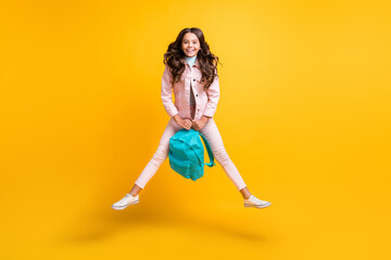 Fototapeta na wymiar Full size photo of brunette wavy haired funky happy girl jump up hold school bag isolated on yellow color background