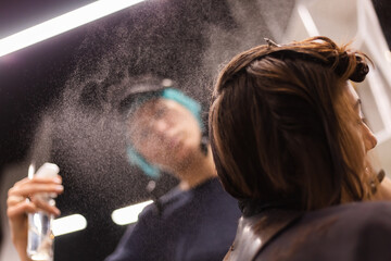 A professional girl hairdresser in face mask makes a client trendy stylish short hair cut. The girl...