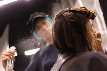A professional girl hairdresser in face mask makes a client trendy stylish short hair cut. The girl...