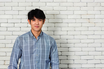 Portrait of Asian handsome young man he smile and looking at camera on brick wall background. Happy guy smiling. Portrait of laughing young man standing with confident