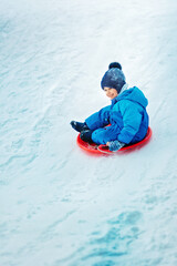 Fototapeta na wymiar child rolls down a snow hill. Boy sliding down snow hill in winter. Kids play outside. Winter fun concept