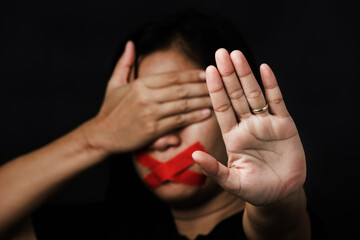 Woman blindfold wrapping mouth with red adhesive tape and show hand sign stop abusing violence and abuse on black background, Human trafficking and abuse, International Human Rights day