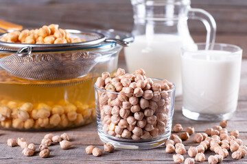 Fresh chickpea milk in glass and pitcher on wooden table. Healthy vegan eating.