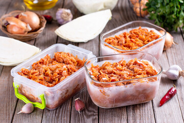 Frozen stewed cabbage in a container on a wooden background for freezing. Frozen food